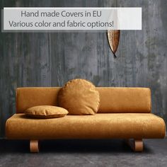 an orange couch with two pillows on it in front of a gray wall that says hand made covers in eu various color and fabric options