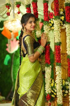 a woman in a green and gold sari standing next to a floral display with red flowers