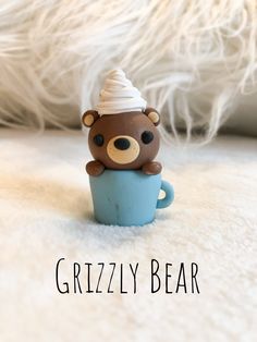 a brown bear sitting in a blue cup with a white hat on its head and the words grizzly bear above it