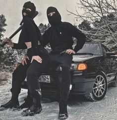 two people sitting on the hood of a car in the snow with skis attached to their heads