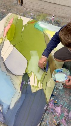 a man is painting on a large piece of paper with acrylic paint and brush