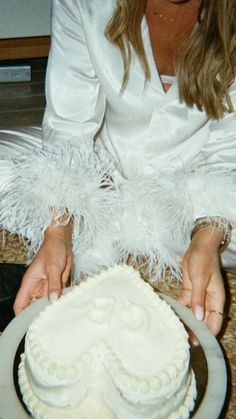 a woman is holding a cake with white frosting and feathers on the top layer