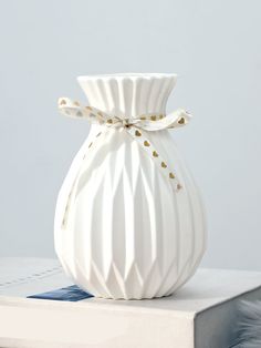 a white vase sitting on top of a table next to a blue and white book