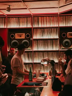 a group of people standing in front of a red counter top with records on it