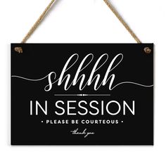 a black sign hanging from a rope with the words shhl in session on it