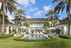 a large white house with palm trees surrounding it and a pool in the foreground