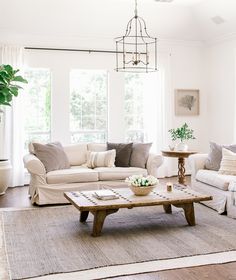 a living room filled with furniture and a chandelier hanging from the ceiling in front of two windows