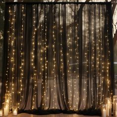 some candles are lit up in front of a sheer curtain with lights on the outside