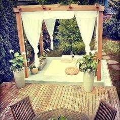 an outdoor patio area with potted plants and white drapes on the side of it