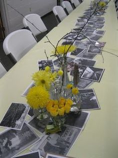 a long table with yellow flowers and pictures on the table, along with white chairs