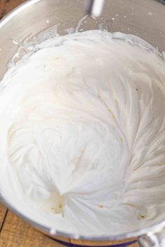 a metal bowl filled with white frosting on top of a wooden table