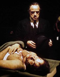 a man in a suit and tie laying on a bed next to another man with blood all over his body