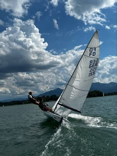 a person riding a sailboat on top of a body of water under a cloudy blue sky