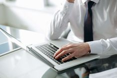 a man is typing on his laptop while wearing a tie and dress shirt, sitting at a glass table