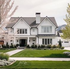 a large white house with lots of windows and grass in front of the door is surrounded by flowering trees