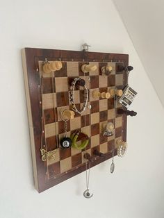 a wooden chess board mounted to the side of a wall with jewelry hanging on it