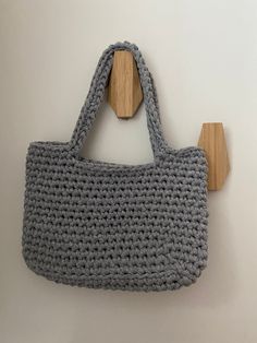 a gray crocheted bag hanging on a wall next to a wooden hanger