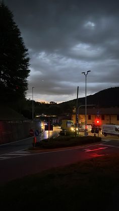 an empty street at night with cars parked on the side and dark clouds in the sky