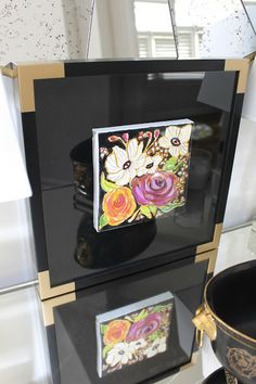 a black and gold box with flowers on it sitting on top of a shelf next to a vase