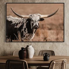 a cow with large horns is standing in the grass near a table and some chairs