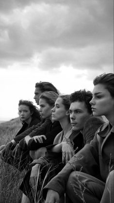 a group of people sitting on top of a grass covered field next to each other