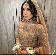 a woman wearing a bridal outfit and holding flowers in front of a wooden wall