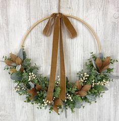 a wreath with greenery and ribbon hanging on a white wooden wall in the shape of a circle