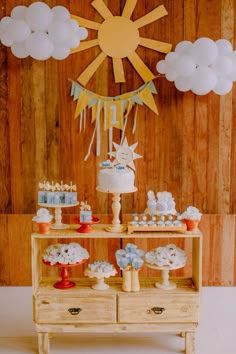 a cake and cupcakes on a table in front of a wooden wall with clouds