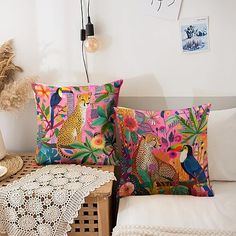 two decorative pillows on a bed next to a table with a doily and lamp