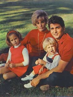 a man and two children sitting on the grass in front of a tree with their arms around each other