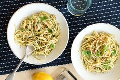 two white bowls filled with pasta on top of a blue and white table cloth next to lemons