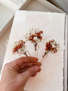 a hand is holding some dried flowers on a piece of paper