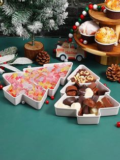 several trays filled with different types of food on a table next to a christmas tree