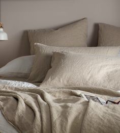 an unmade bed with two pillows and a book on the pillowcase next to it