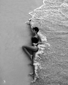 black and white photograph of a woman laying on the beach with her legs in the water