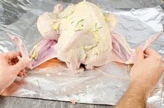 two hands are peeling an uncooked chicken on aluminum foil, with the skin still attached