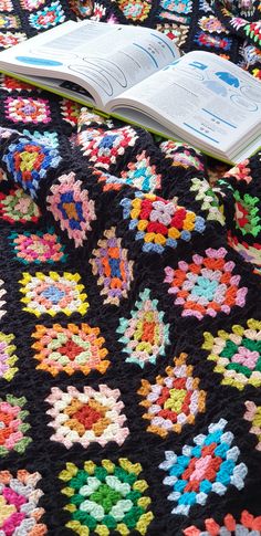 an open book laying on top of a crocheted blanket covered in multicolored flowers