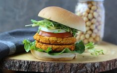 a chicken burger with lettuce and tomato on a wooden board next to corn