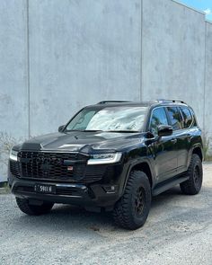 a black suv is parked in front of a building with concrete walls and gravel on the ground