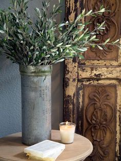 a vase filled with greenery sitting on top of a table next to a candle