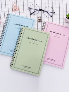 three notebooks sitting next to each other on top of a white table with glasses