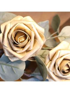 two white roses with green leaves on a table