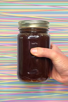 a hand is holding a jar of jam on a multicolored striped tablecloth