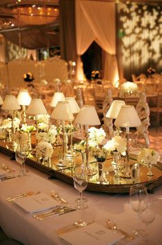 the table is set with white flowers and goldware for an elegant dinnereon party