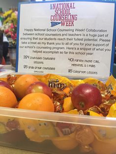 there are oranges and apples in a plastic container on the table with a sign