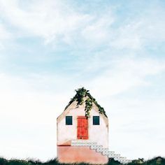 a small house sitting on top of a lush green hillside next to a red door