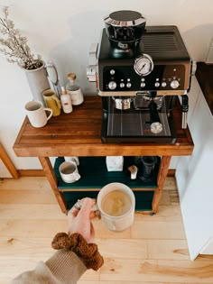 a person holding a coffee cup in front of an espresso machine on a wooden table