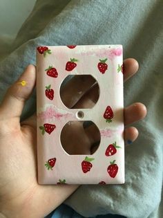 a person holding a pink and white light switch cover with strawberries on it,