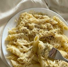 a white plate topped with pasta covered in cheese and seasoning next to a fork