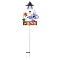 a welcome sign with butterflies on it and a street light attached to the pole that says welcome